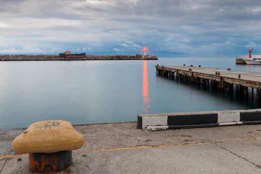 Embankment, pier and lighthouse with bright red light on the seashore at dusk