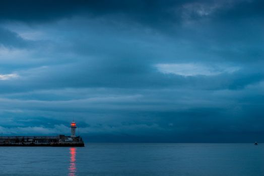 Beautiful lighthouse on the seashore at dusk, rainy clouds over the sea