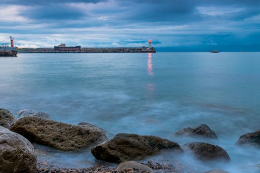 view of the lighthouse on the seashore at dusk, rainy clouds over the sea