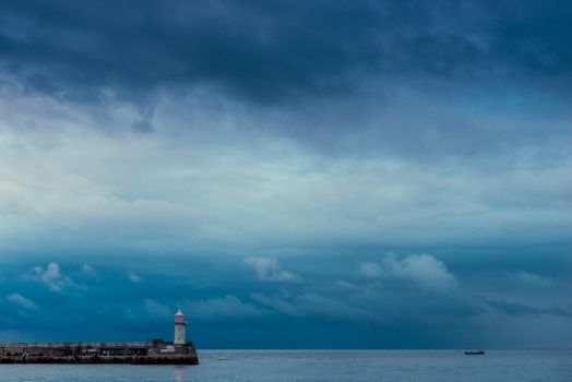 Lonely lighthouse with a red lantern on a background of rainy blue clouds over the sea