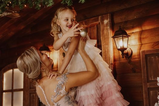 Young beautiful mother holds a little daughter who decorates a Christmas tree in the fairy room