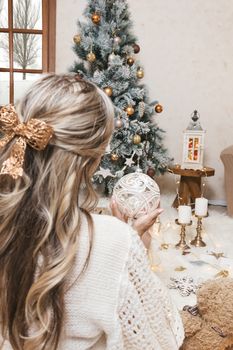 A woman holds a large glittering crystal bauble in front of the tree at Christma time