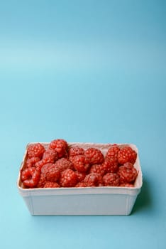 box of fresh raspberries on a blue background