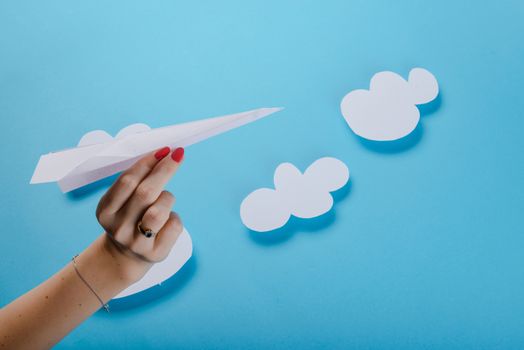 Paper plane in female hand on a blue background with clouds