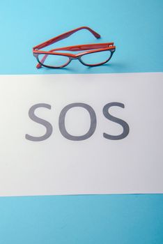 Word SOS written on white paper. Blue background