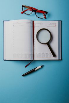 Business planning with copy space and office supplies. Magnifying glasses and red glasses on blue background