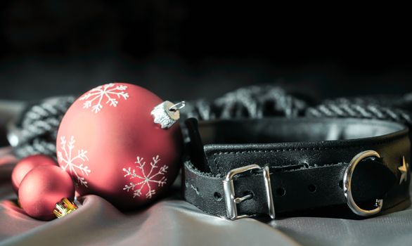 bdsm still life black leather collar and red christmas balls on silver fabric close up