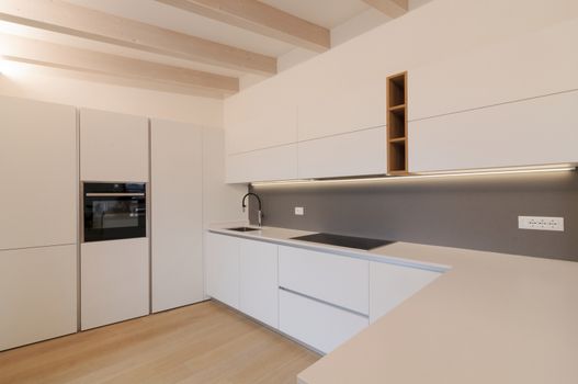 Modern and elegant kitchen interior with white cabinets, induction hob and wooden inserts. Contemporary Scandinavian style