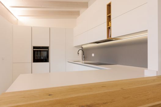 Modern and elegant kitchen interior with white cabinets, induction hob and wooden inserts. Contemporary Scandinavian style