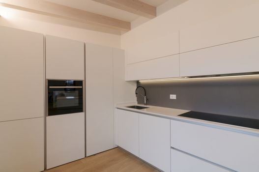 Modern and elegant kitchen interior with white cabinets, induction hob and wooden inserts. Contemporary Scandinavian style