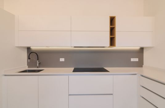 Modern and elegant kitchen interior with white cabinets, induction hob and wooden inserts. Contemporary Scandinavian style