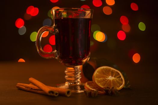 Mulled wine with cinnamon sticks and orange over holiday christmas lights background