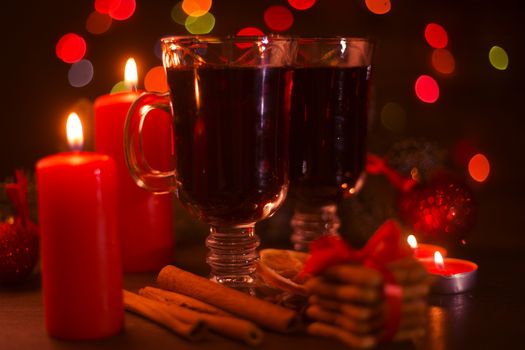 Mulled wine with cinnamon sticks orange candles fir tree branch and baubles over holiday christmas lights background