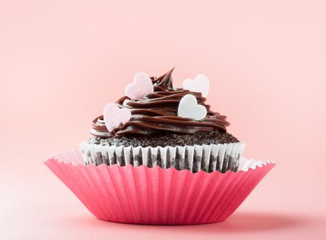 chocolate cupcake with chocolate icing and eatable hearts, in nice decorative paper mold, pink background