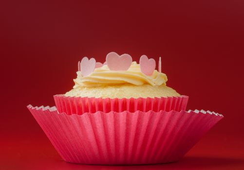Vanilla cupcake with eatable hearts on vanilla icing, red background