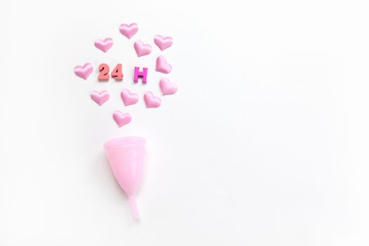 Pink menstrual cup on white background with hearts and designation of use time, 24 hours, laid out in colored numbers and letter. Concept zero waste, savings. Flat lay, copy space. Horizontal.