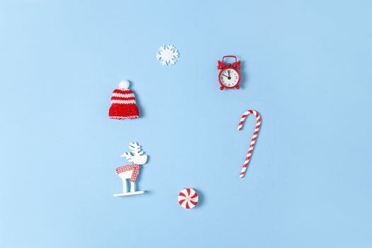 Simple creative Christmas composition. Candy cane, deer, hat, snowflake, red clock on blue background, copy space. Minimal style. Top view. Horizontal. For greeting card, office supplies.