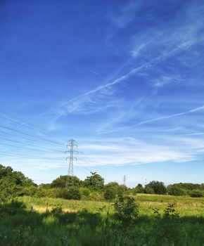 High voltage pylons and lines in a rural landscape against a blue sky. green country landscape on a sunny day. Association of agriculture and industry in one photo. Beautiful spring landscape of the European plain. high voltage electric wire pole tower, the beautiful sky, and the cloud in Poland