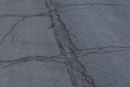 Asphalt road surface with small cracks and damages. Sidewalk asphalt road with cracks. Floor. Texture of tarmac road with cracks. Abstract background