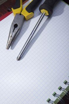 Screwdriver and pliers on a checkered notebook