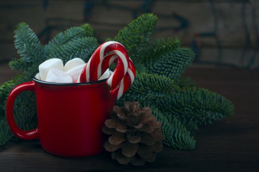 Cocoa in red mug with marshmallows and candy cane and Christmas fir tree on dark wooden background