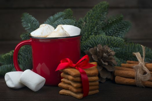 Cocoa in red mug with marshmallows and candy cane Christmas fir tree and gingerbread cookies on dark wooden background