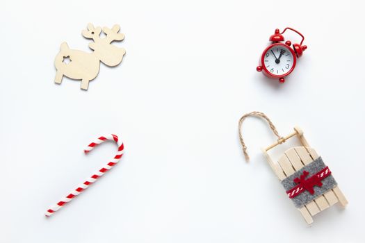 Christmas flat lay, wooden deer, candy cane, small red analog clock, sled on white background, copy space. Minimal style. Top view. Celebration, festive, eco concept. Horizontal.