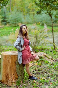 Woman standing next to a tree in park in golden autumn.