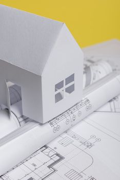 White family paper house over block of flats on yellow background paper. Minimalistic and simple concept, style. Copy space. Vertical orientation.