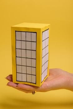 White family paper house over block of flats on yellow background paper. Minimalistic and simple concept, style. Copy space. Vertical orientation.