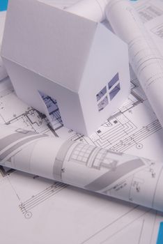 White family paper house, house projects plan and blueprints in the background. Minimalistic and simple concept, style. Horizontal orientation. View from above.