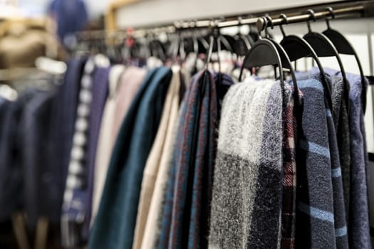 Soft winter scarves in different colors hang on hangers in the store. Blurred background.