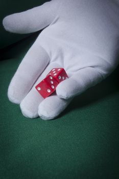 Hand in a white glove throwing red dice on the table