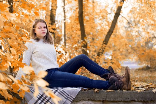 Beautiful teenager girl sitting in autumn garden on the fence , on woolen plaid blanket