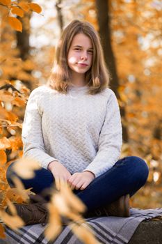 Beautiful teenager girl sitting in autumn garden on the fence , on woolen plaid blanket