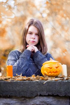 Beautiful teenager girl in autumn garden with halloween pumpkin and candles