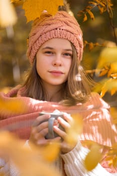 Portrait of pretty nice teenage girl drinking hot cocoa with marshmallows in autumn park