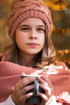 Portrait of pretty nice teenage girl drinking hot cocoa with marshmallows in autumn park