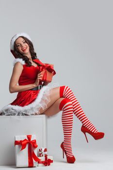 Beautiful young pin-up girl in santa dress sitting near christmas presents