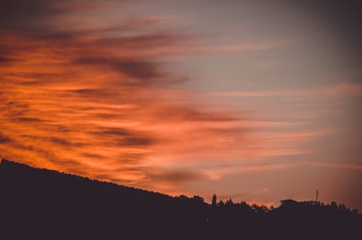 Some intense red and orange clouds reach the shadows of the gound while sunset arrives