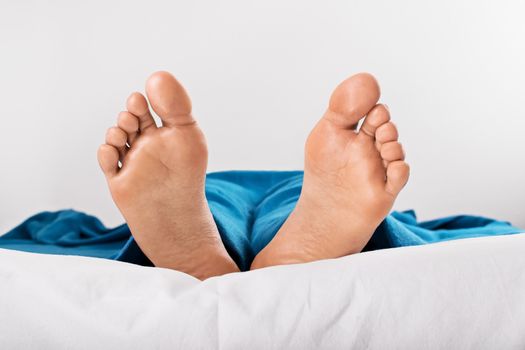Close up shot of female feet under blue blanket, isolated on white background.