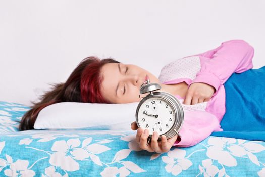 Young woman sleeping in bed, holding an alarm clock. Young woman fallen asleep with alarm clock in her hand. Oversleep, not enough sleep concept.