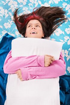 Cute young woman in pink pajamas lying in bed, smiling and hugging her pillow. Rest, sleeping, comfort and people concept. Top view.