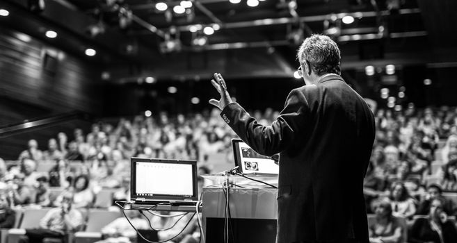 Speaker giving a talk on corporate business conference. Unrecognizable people in audience at conference hall. Business and Entrepreneurship event. Black and white image.