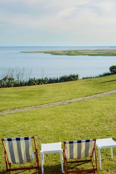 Empty beach chair on meadow on summer time. Sunlight and sea in the background. Coast line