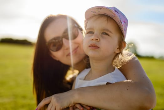 Happy mother and daughter in the park. Beauty nature scene with family outdoor lifestyle. Happy family resting together on the green grass, authentic lifestyle image