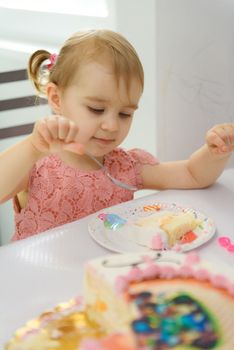 Baby girl 1 year old eating birthday cake in room. Birthday party. Childhood.