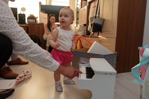 beautiful baby girl playing toy piano in light room. Authentic image.