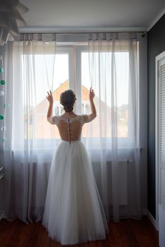Bridesmaid helping slender bride lacing her wedding white dress, buttoning on delicate lace pattern with fluffy skirt on waist. Morning bridal preparation details newlyweds. Wedding day moments, wear.