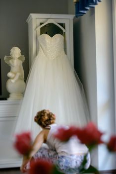 Bridesmaid helping slender bride lacing her wedding white dress, buttoning on delicate lace pattern with fluffy skirt on waist. Morning bridal preparation details newlyweds. Wedding day moments, wear.